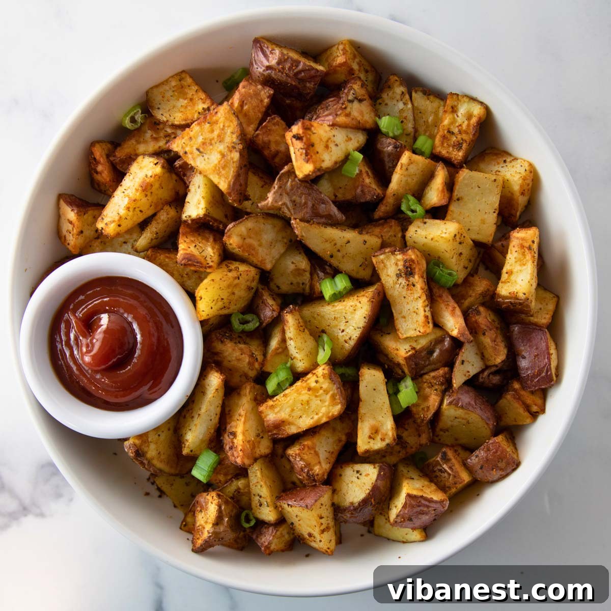 Crispy Air Fryer Red Potatoes 2 A vibrant bowl of crispy air fryer red potatoes, garnished with fresh herbs and ready to serve, with a small cup of ketchup beside it.