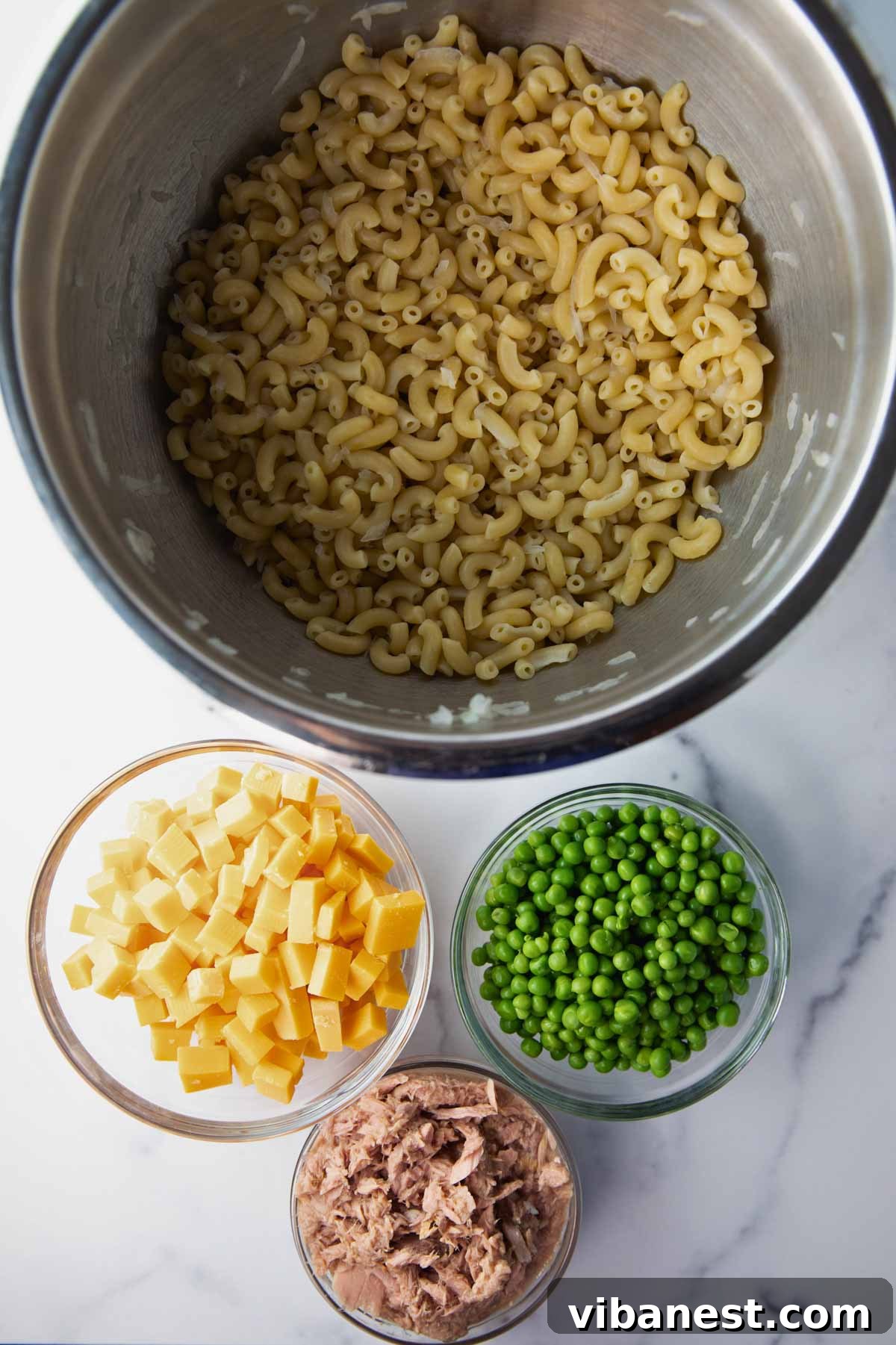 Quick Creamy Tuna Macaroni Salad 4 Collection of fresh ingredients for tuna macaroni salad, including cooked macaroni, drained tuna, cubed cheddar cheese, and bright green peas.