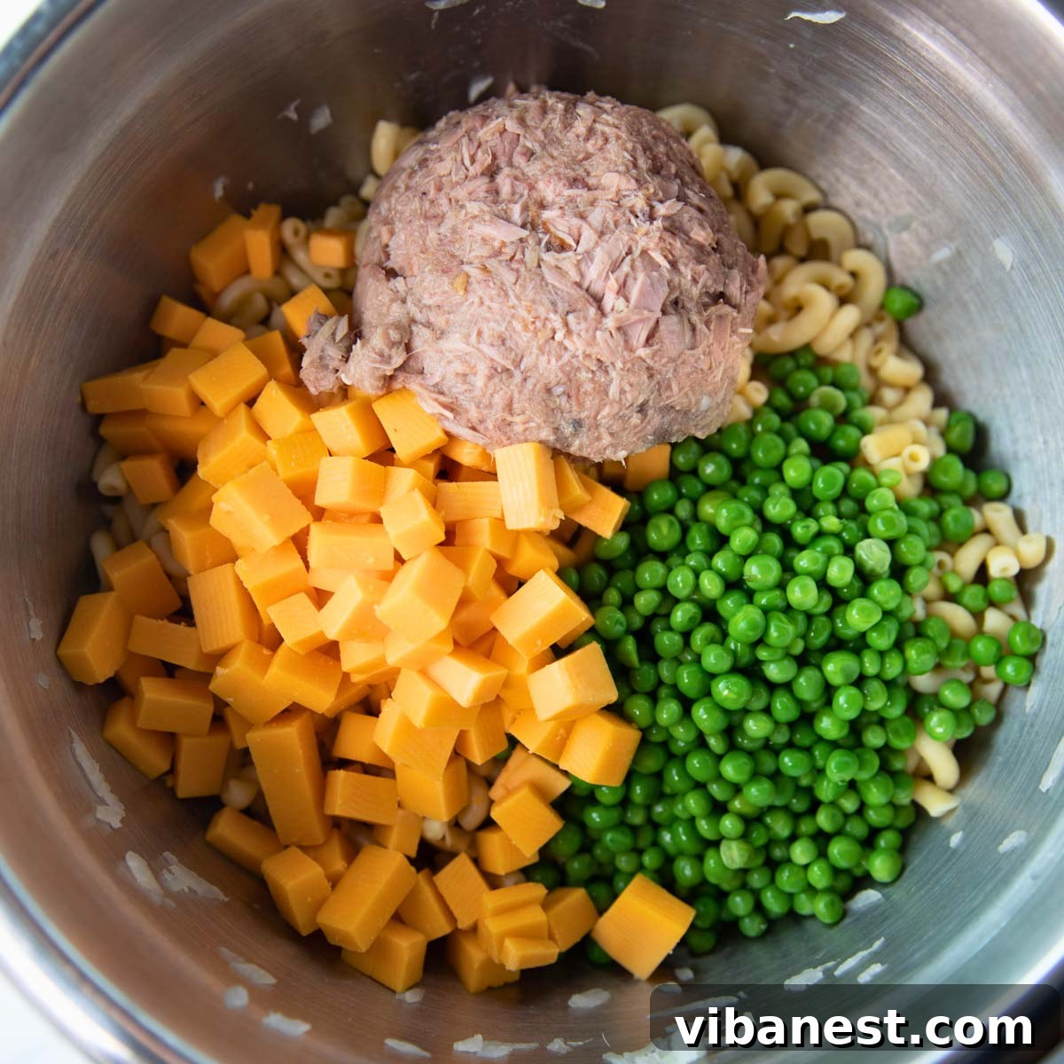 Quick Creamy Tuna Macaroni Salad 5 A large mixing bowl containing drained tuna, vibrant cheddar cheese cubes, and bright green peas, ready to be combined with macaroni.