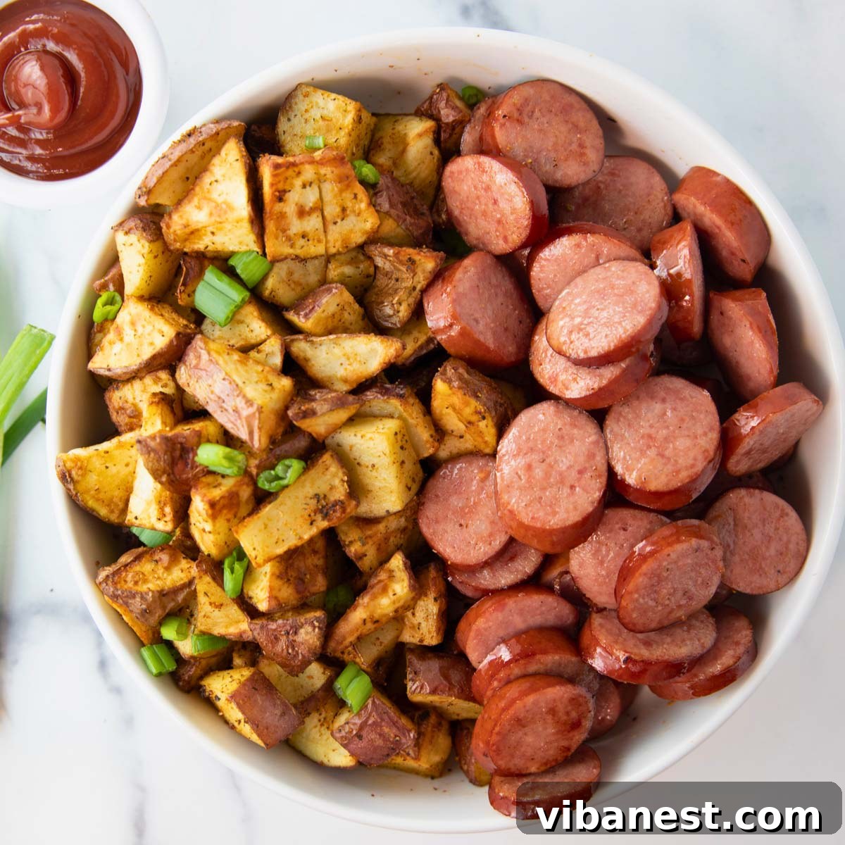 Smoky Air Fryer Sausage and Crispy Potato Medley 2 Overhead view of a bowl of crispy air fryer smoked sausage and potatoes, with a side of ketchup.