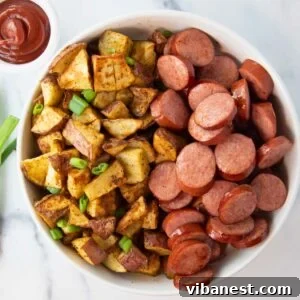 Overhead view of a bowl of crispy air fryer smoked sausage and potatoes with a side of ketchup.