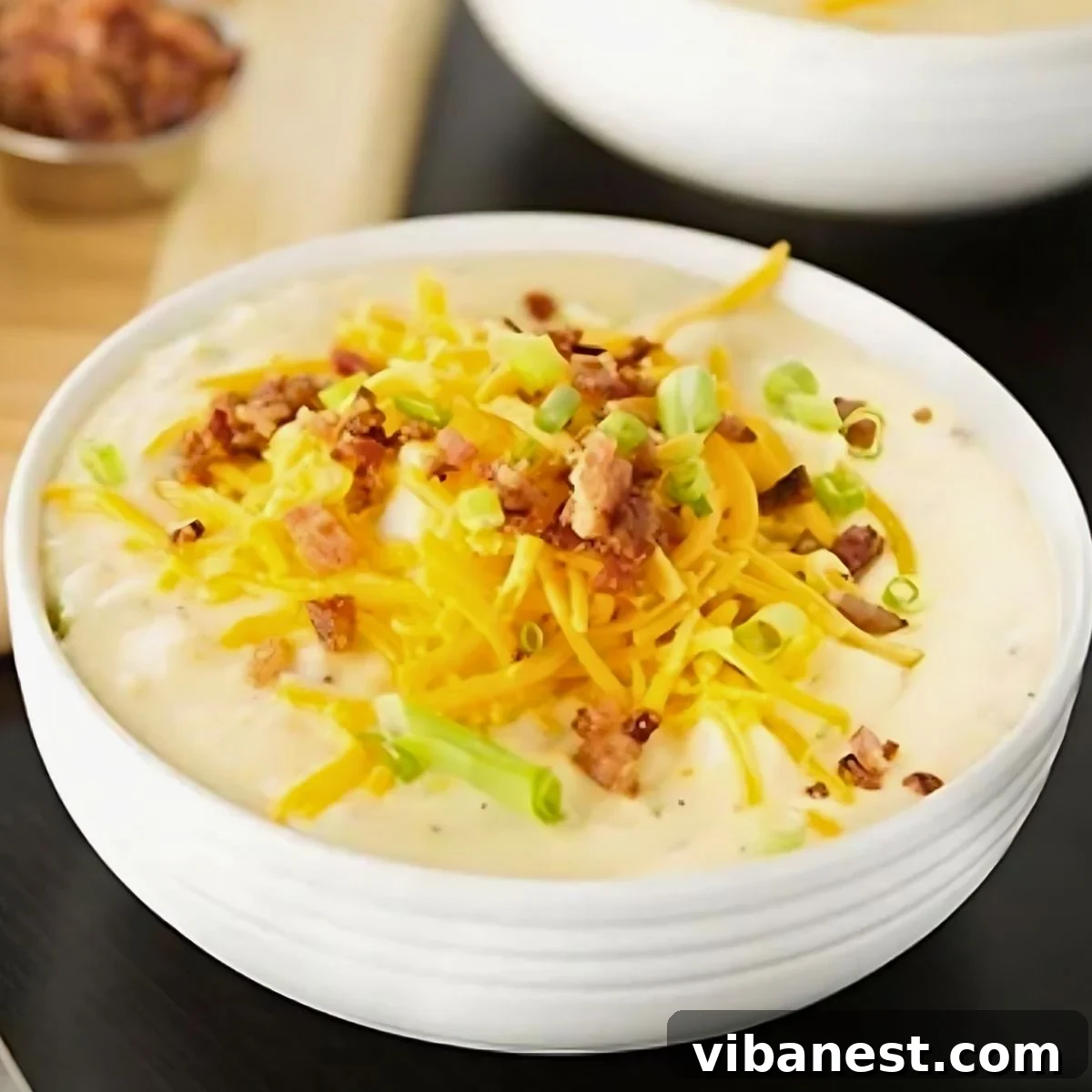 The Definitive Loaded Potato Chowder 2 A steaming bowl of loaded baked potato soup, garnished with bacon, cheese, and green onions.