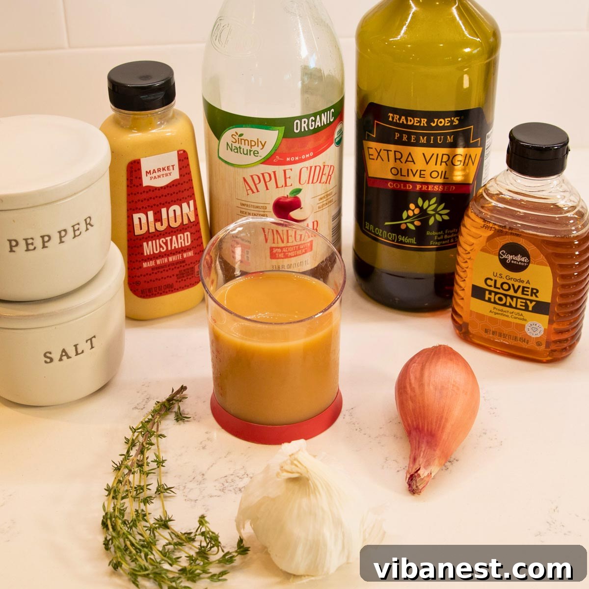 Crisp Apple Vinaigrette 4 Ingredients laid out for apple cider vinaigrette: fresh apple cider, apple cider vinegar, olive oil, honey, shallot, garlic, dijon mustard, salt, fresh thyme, and black pepper.