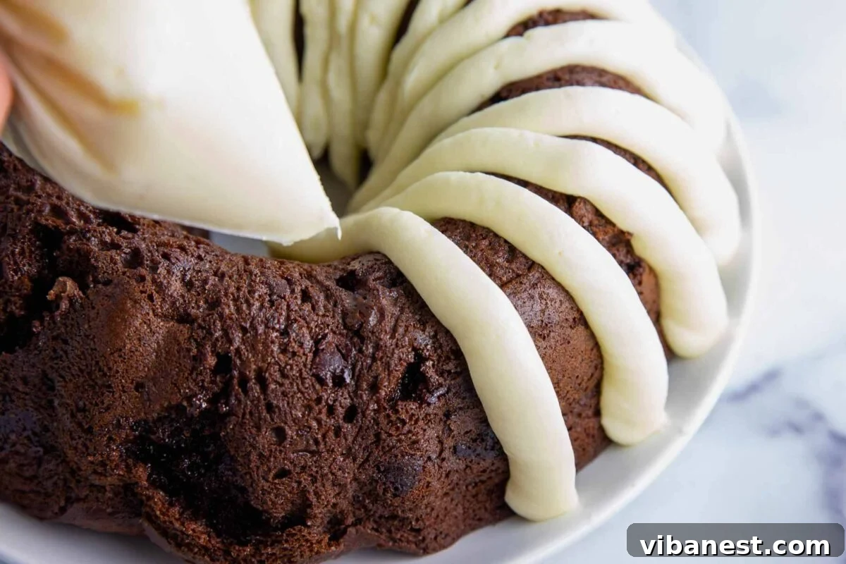 Decadent Double Chocolate Bundt Cake 16 A baker expertly piping thick, elegant ribbons of creamy cream cheese frosting onto a cooled chocolate bundt cake, mimicking the classic Nothing Bundt Cake style with a Ziplock bag.