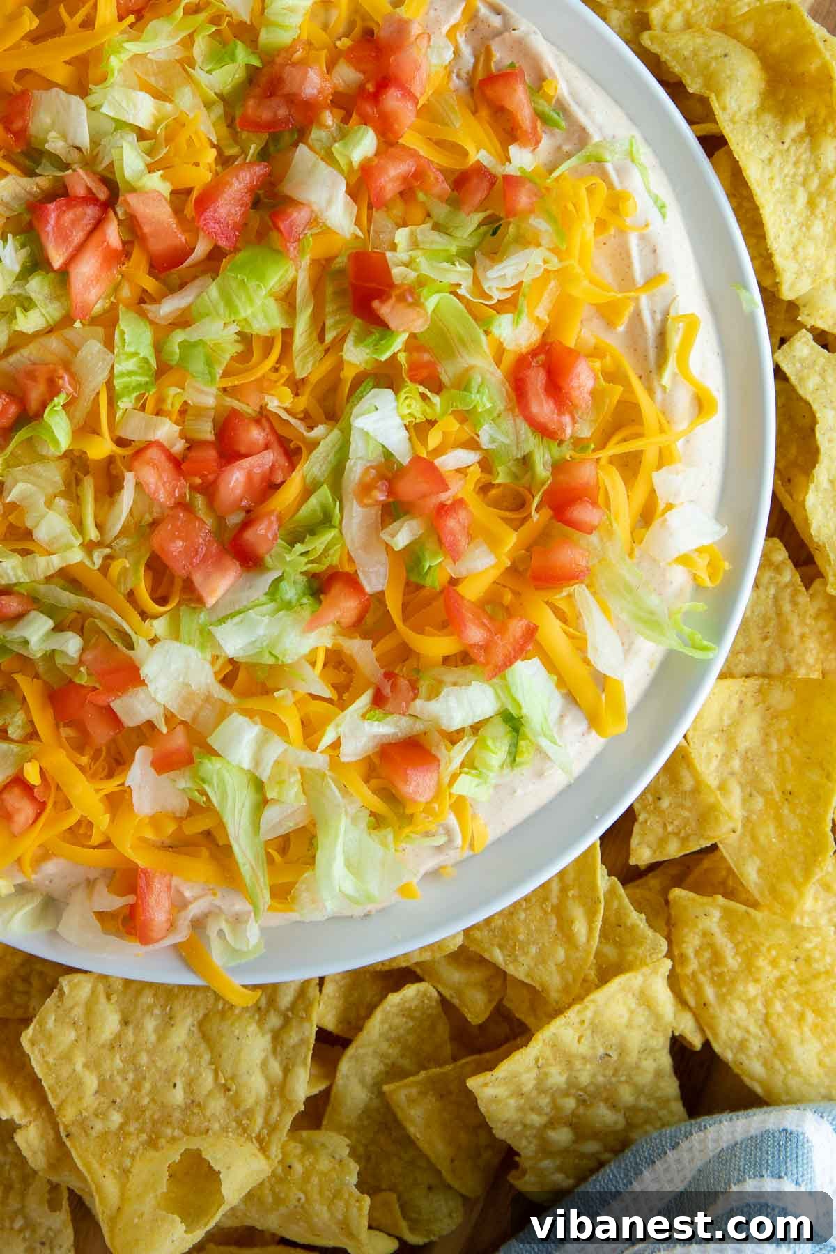 Ultimate Taco Party Dip 7 A large, vibrant taco dip appetizer arranged on a table, surrounded by an abundance of tortilla chips, ready for a party.