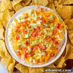 Vibrant taco dip made with a creamy base of cream cheese, sour cream, and taco seasoning, topped with fresh ingredients.