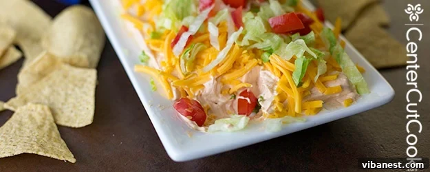 taco dip.jpg Close-up of a beautifully layered taco dip with vibrant toppings, ready to be enjoyed with tortilla chips.