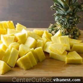 Tropical Berry Bliss 3 Freshly cut pineapple pieces on a wooden cutting board, ready for use in a smoothie or other recipes.