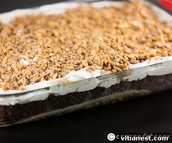 Decadent and Easy No-Bake Toffee Dessert A slice of Better Than Sex Cake on a white plate, revealing the moist chocolate cake base soaked in caramel, topped with Cool Whip and toffee bits.