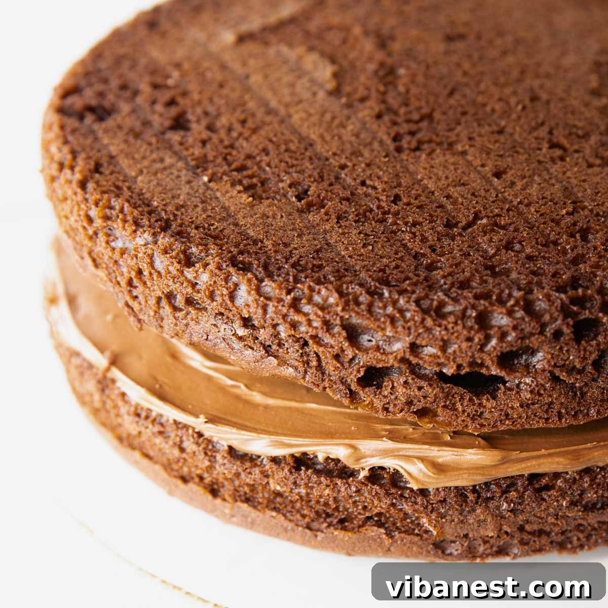Savor Portillos Legendary Chocolate Cake 11 A two-layer chocolate cake being frosted with chocolate frosting