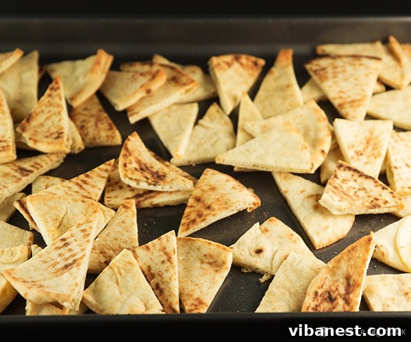 Seasoned Pita Chips on Baking Sheet Pita triangles tossed with olive oil and seasonings on a baking sheet, ready for the oven.