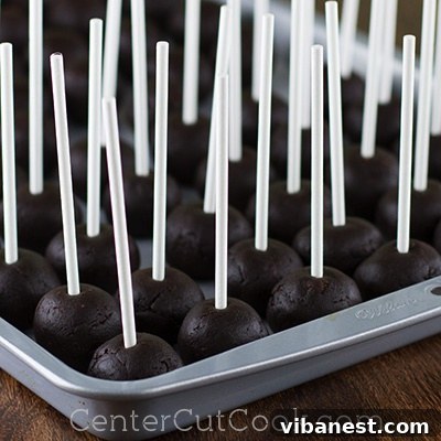 Close-up photo of several cake balls with lollipop sticks securely inserted, arranged on a baking sheet, ready for the next chilling phase.