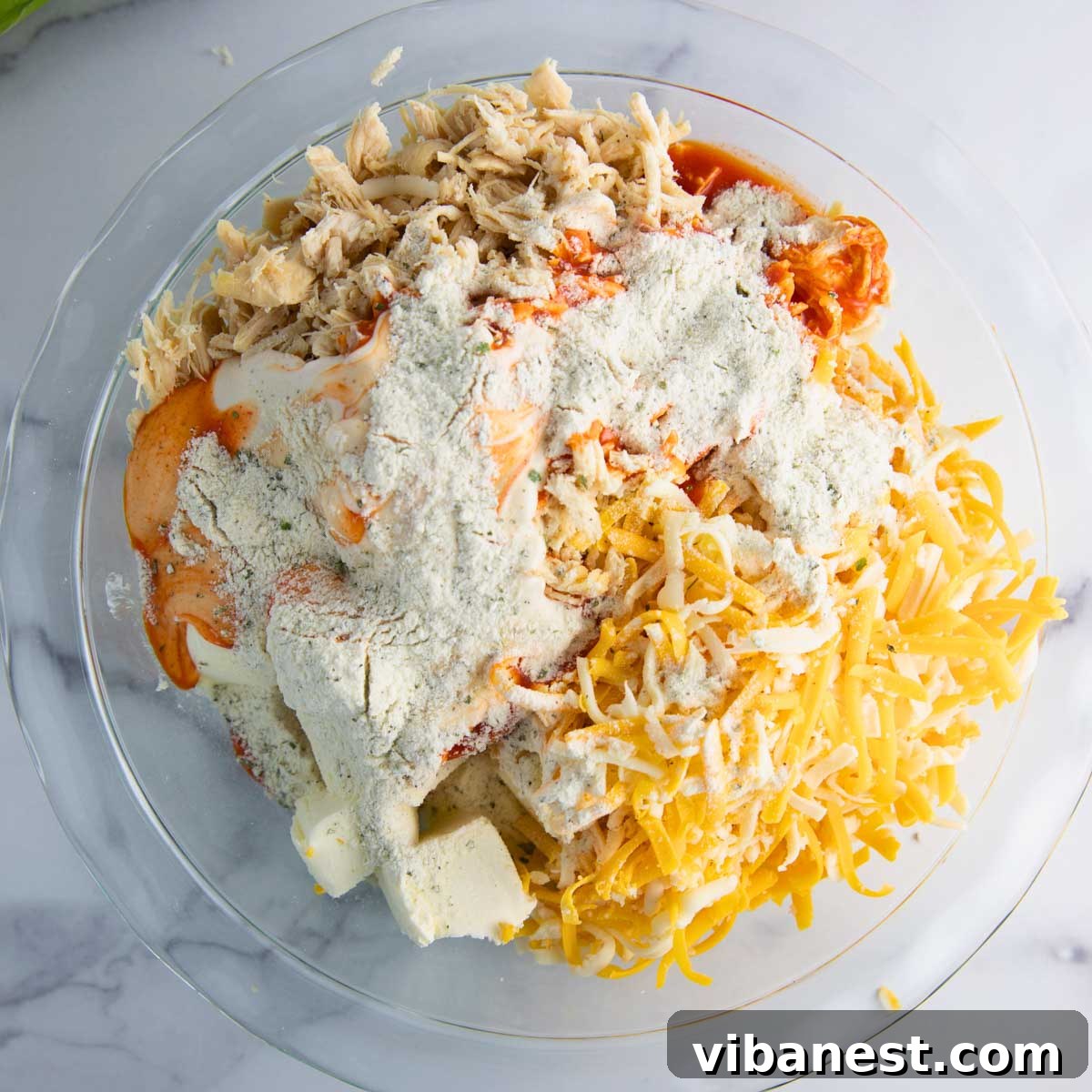 Ultimate Tangy Chicken Dip 6 ingredients for buffalo chicken dip in a baking dish ready to be baked.
