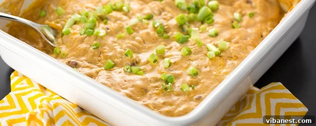 Cheesy Bean Dip ready to enjoy Top-down view of cheesy bean dip with a scoop taken out, served with an abundance of crispy tortilla chips on a rustic wooden surface