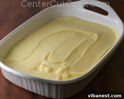 Smooth, creamy Chess Cake topping being spread evenly over the pre-baked yellow cake mix crust, showing the seamless transition of layers before baking.