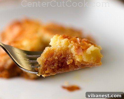 A close-up shot of a single square of Chess Cake, revealing the distinct chewy yellow cake mix crust and the rich, creamy, custard-like top layer, dusted with powdered sugar.