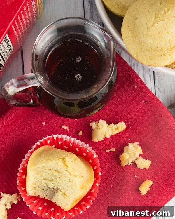 kid-friendly-pancake-muffins A child's hands dipping a pancake muffin into a small cup of maple syrup.
