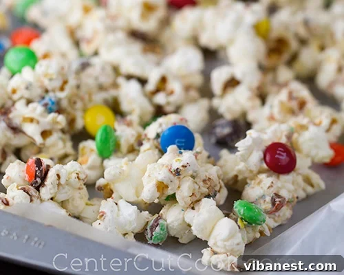 Popcorn being mixed with melted white chocolate, M&M's, and sea salt in a large bowl
