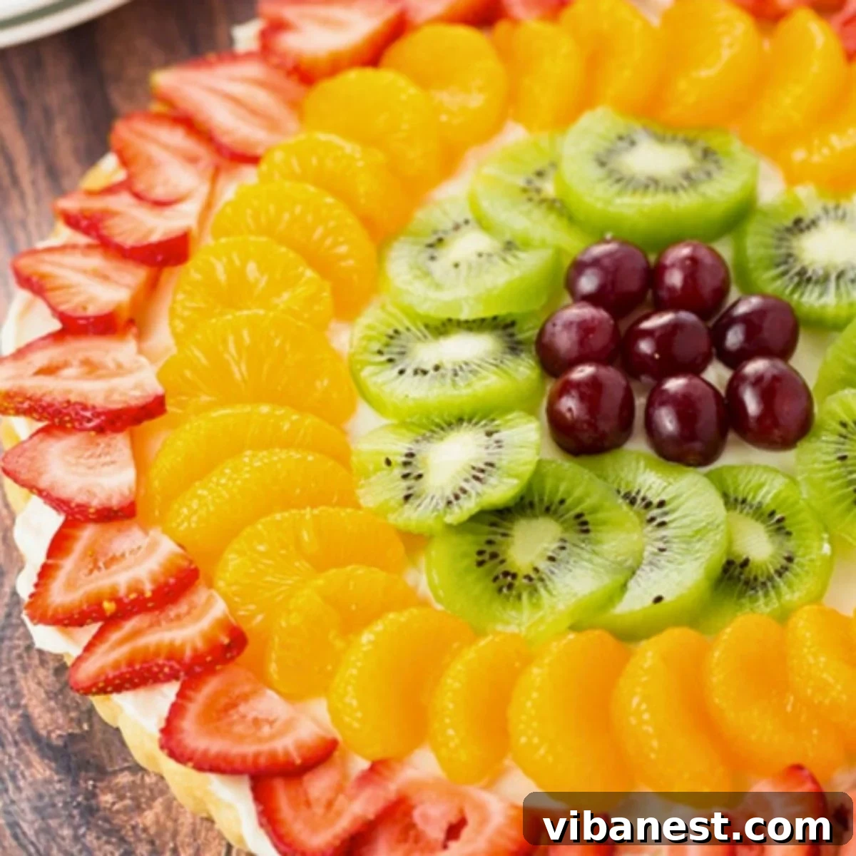Rainbow Fruit Dessert Pizza 2 close-up of colorful fruit pizza made with a sugar cookie crust, cream cheese frosting and topped with fresh fruit: strawberries, oranges, kiwi and grapes.