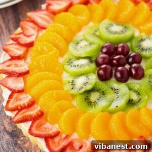 close-up of colorful fruit pizza made with a sugar cookie crust, cream cheese frosting and topped with fresh fruit: strawberries, oranges, kiwi and grapes.