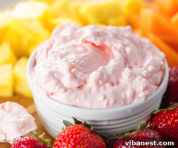 Fruit Dip with Assorted Fresh Fruits for Serving Fruit dip in a small elegant white bowl, thoughtfully placed on a rustic wooden serving board alongside a colorful assortment of fresh fruits like golden pineapple chunks, bright red strawberries, and luscious green grapes